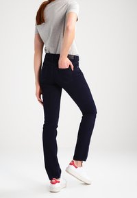 Mörkblå jeans med slim fit, fem fickor och en lätt urtvättad textur, kombinerat med en grå t-shirt och vita sneakers.