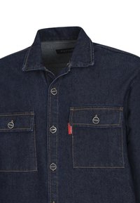 Camisa de mezclilla azul oscuro con cuello, con bolsillos delanteros, botones plateados y costuras visibles en un tono amarillo contrastante.