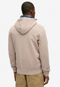 Light beige hoodie with a drawstring, soft texture, and kangaroo pocket, layered over a blue denim shirt. Simple design, casual fit.