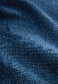 Primer plano de tela vaquera azul que muestra la textura detallada del tejido y los pliegues naturales.