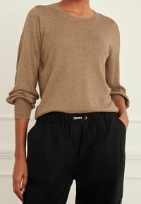 Pull en tricot marron chiné avec un col rond et des manches retroussées, associé à un pantalon noir à cordon de serrage avec des poches latérales.
