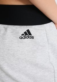 Grijze joggingsbroek met een visgraatpatroon, voorzien van een zwarte elastische tailleband en een zwart Adidas-logo aan de zijkant.