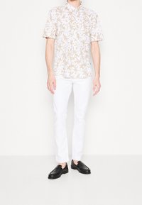 Camicia a maniche corte con colletto, sfondo bianco e motivo floreale marrone chiaro, abbinata a pantaloni slim-fit bianchi e mocassini neri.