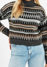 Strickpullover mit Rollkragen, geometrischen Mustern in Schwarz, Grau, Weiß und Braun, mit einer strukturierten Oberfläche sowie einem gerippten Saum und Bündchen.