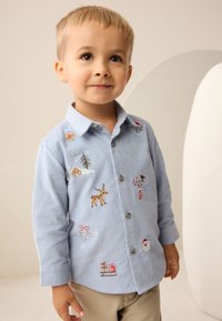 Hellblaues Cordhemd mit detaillierter Stickerei von Feiertagsmotiven, darunter ein Rentier, ein Schneemann, Geschenke und festliche Bäume.