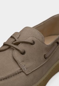 Παπούτσι από ανοιχτό καφέ σουέντ με στρογγυλεμένη μύτη, δέσιμο με κορδόνια και διακριτικές ραφές. Εξωτερική σόλα από καουτσούκ με πλευρικές εγκοπές για αερισμό.