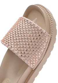 Slip-on sandaal met een gestructureerde beige rubberen zool. De bovenkant heeft een gaasontwerp versierd met kleine, roségouden accenten.