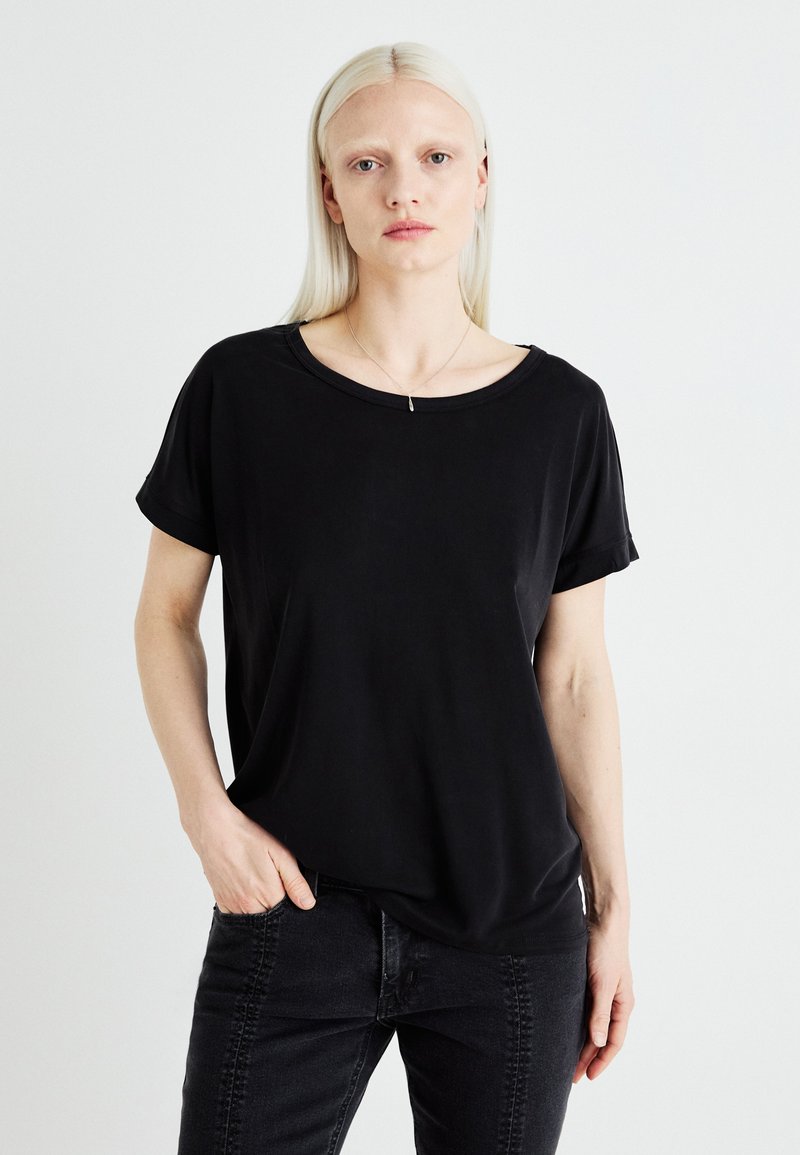 Black short-sleeve T-shirt with a relaxed fit, round neckline, and soft texture, paired with dark jeans. Simple, versatile design.