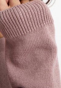 Détail de pull en maille de couleur mauve douce avec poignets côtelés. Texture lisse et couture uniforme, mettant en valeur l'élasticité et la douceur du tissu.