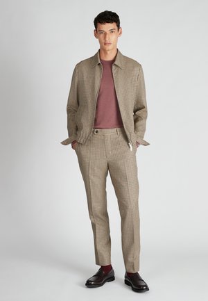 Veste de costume à carreaux marron avec pantalon assorti, accompagnée d'une chemise bordeaux. Tissu lisse, design structuré et poches latérales. Chaussures sombres.