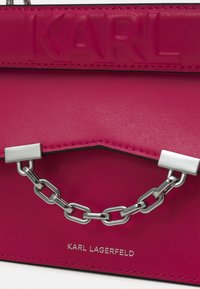 Różowa skórzana torebka z tłoczonym logo "KARL", srebrnym łańcuszkiem, usztywnioną formą oraz kontrastowym przeszyciem. Posiada zapięcie na klapę.