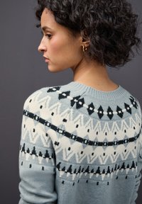 Maglione lavorato a maglia blu chiaro con motivi geometrici in bianco e nero. Collo rotondo e maniche lunghe con polsini a costine.
