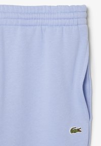 Helle blaue Stoffhose mit elastischem Taillenbund und Seitentasche, mit einem kleinen grünen Krokodil-Logo nahe der Tasche.