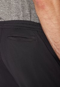 Shorts de sport noirs avec une taille élastique et une poche arrière plate et inclinée. Le tissu semble lisse avec une finition légèrement mate.