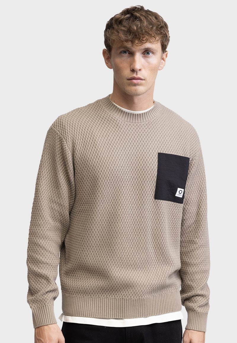 Maglione beige a maglia con un motivo testurizzato, polsini e orlo a coste, e una tasca nera con dettagli del logo sul lato sinistro del petto.