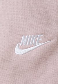 Light pink fabric features an embroidered white Nike logo, showcasing a smooth texture and clear branding with the iconic swoosh design.