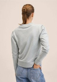 Lysegrå sweatshirt med lange ærmer, rund hals og ribbet kant, med let puffede skuldre, kombineret med blå denimjeans.