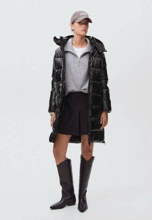 Cappotto a piuma nero, felpa grigia con zip, gonna nera e stivali neri al ginocchio. Cappello grigio con scritta bianca. Aspetto complessivo sportivo.