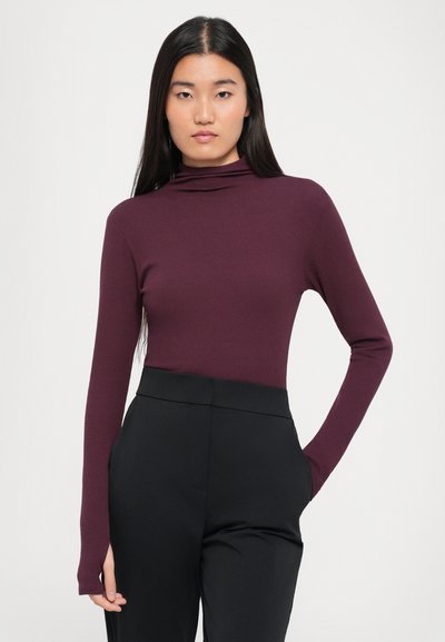 Burgundy long-sleeve mock neck top made of stretchy fabric, paired with high-waisted black trousers featuring side pockets.