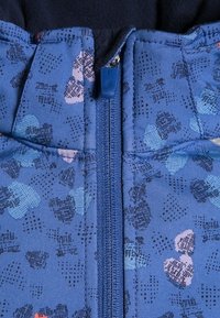 Veste zippée bleue avec un motif floral en rose clair et bleu foncé. Tissu texturé avec une fermeture éclair lisse et un doublure contrastante bleu marine.