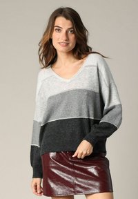 Pull gris rayé avec décolleté en V, tissu doux et coupe ample. Associé à une mini-jupe bordeaux brillante.