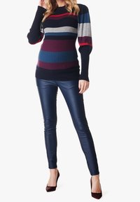 Suéter de punto con rayas multicolores en azul marino, burdeos, gris y verde azulado; combinado con pantalones ajustados de piel sintética azul marino y tacones burdeos.