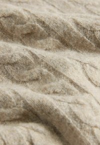 Beige knitted fabric featuring a textured cable pattern. The surface appears soft and fuzzy, with subtle variations in color and depth.