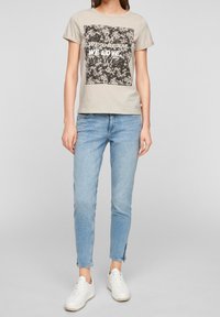 Šedé bavlněné tričko s čtvercovým grafickým potiskem v černobílém textu. V kombinaci se světle modrými džíny a bílými teniskami.