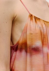 Verstelbare spaghettiband tanktop in een verloop van oranje, roze en wit, met zachte, vloeiende stof en een lichte glans.