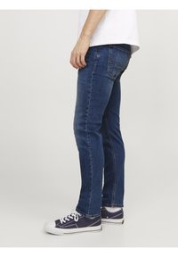 Mörkblå denimjeans med slim fit och femficksdesign. Har synlig sömnad och en logotyp patch bak. Bärs med marinblå sneakers.