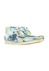 Botas chukka multicolores con un patrón de tie-dye en tonos de azul, verde y amarillo, con un suave upper de ante y cordones blancos.