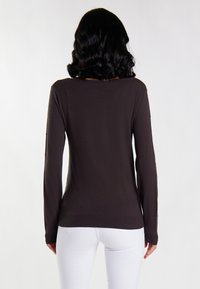 Brauner, langärmeliger Pullover mit einem strukturierten, gepunkteten Muster; taillierter Schnitt mit weitem Halsausschnitt und geripptem Saum. Trägt man mit weißen Hosen.
