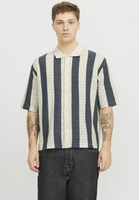 Camicia a maniche corte con strisce zigzag alternate blu scuro e crema, con colletto e chiusura a bottoni.