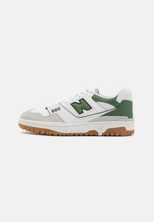 Weißer und grauer New Balance 550 Sneaker mit grünen Akzenten und Kautschuksohle, Seitenansicht vor einfarbigem Hintergrund.