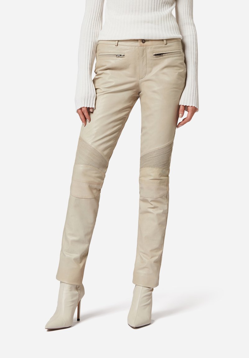 Beige Lederhosen mit gerippten Akzenten und Reißverschlusstaschen, mit schlankem Schnitt und zulaufenden Beinen, kombiniert mit weißen High-Heel-Stiefeletten.