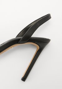 Sandale haute en cuir noir, avec un design élégant, des fines brides et un bout pointu. Le talon est fin et mesure environ 10 cm.