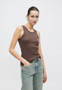 Top de tirantes marrón acanalado con escote redondo y un pequeño logo, combinado con vaqueros de pierna ancha de color azul claro. Diseño simple y casual.