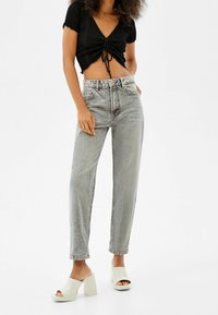 Jeans grigi di stile vintage con vita alta, gamba dritta e orlo leggermente sfrangiato. Abbinati a un top nero corto e mule bianche con tacco spesso.