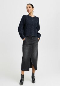 Pletený tmavě námořnický zkrácený kardigan s kulatým výstřihem a knoflíkovým zapínáním, doplněný o černou denimovou sukni s vysokým pasem a předním rozparkem.