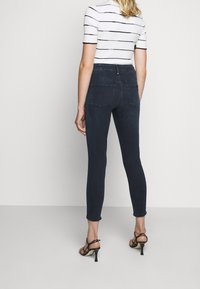 Jeans skinny azul oscuro de cintura alta con cinco bolsillos, combinados con una blusa blanca de manga corta a rayas y tacones negros con tiras.