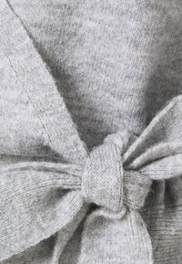 Grått stickat tyg med en mjuk textur, med en knuten rosett som detalj för stil. Designen inkluderar en blandning av ljus och mörkgrå garn.