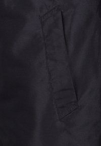 Gros plan d'un tissu noir avec une ouverture de poche rectangulaire cousue sur le côté droit.
