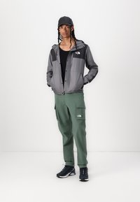 Gray windbreaker with black accents, green cargo pants, and black athletic shoes. The jacket features a hood and buttons down the front.