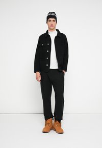 Mustast teksajakirjast jope hõbedaste nööpidega, valge kõrge kaelusega kampsun, mustad püksid ja beežid saapad. Mütsil on must-valge mustriga kujundus.