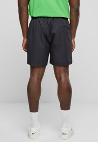Svarte shorts med elastisk midje og en baklomme, kombinert med hvite joggesko og hvite sokker, mot en nøytral bakgrunn.