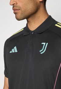 Black polo shirt with a textured fabric, featuring mint green and yellow accents on the shoulders, and a logo on the chest.