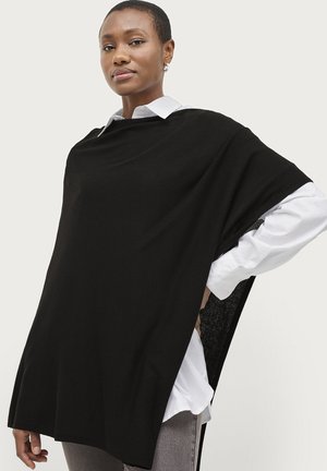 Sort poncho-lignende top lavet af struktureret stof, med brede ærmer og sidelukninger. Bæret over en hvid skjorte med krave.