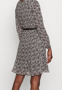 Bloemrijk patroon jurk met lange mouwen, zwart-wit kleurenschema, elastische taille en een zwarte riem. Vloeiende stof met een zoom boven de knieën.