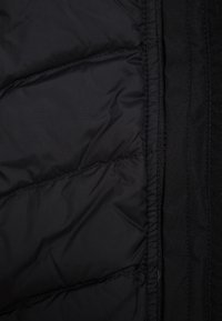 Intérieur d'une doudoune noire avec un design matelassé, une texture lisse, et une fermeture éclair sur le côté droit. Isolation chaude visible.