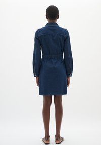 Donkerblauwe denim shirt jurk met een getailleerde taille, lange mouwen en een elastische achterkant. Strakke lijnen en zichtbare stiksels accentueren het geheel.